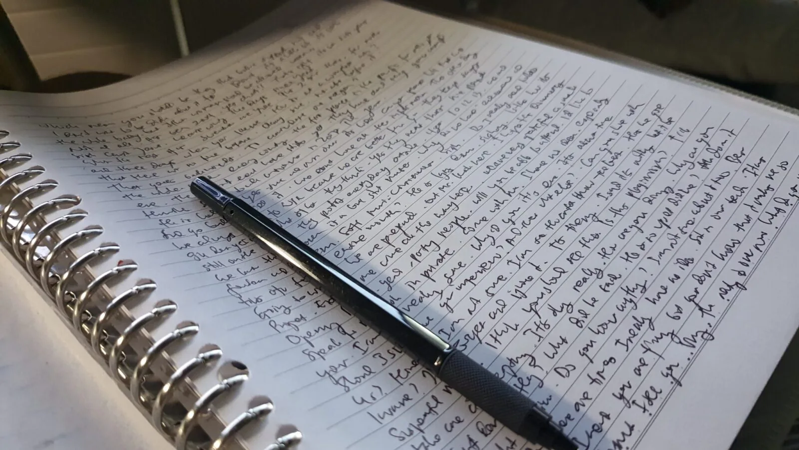 Handwritten pages and a pen resting on a notebook